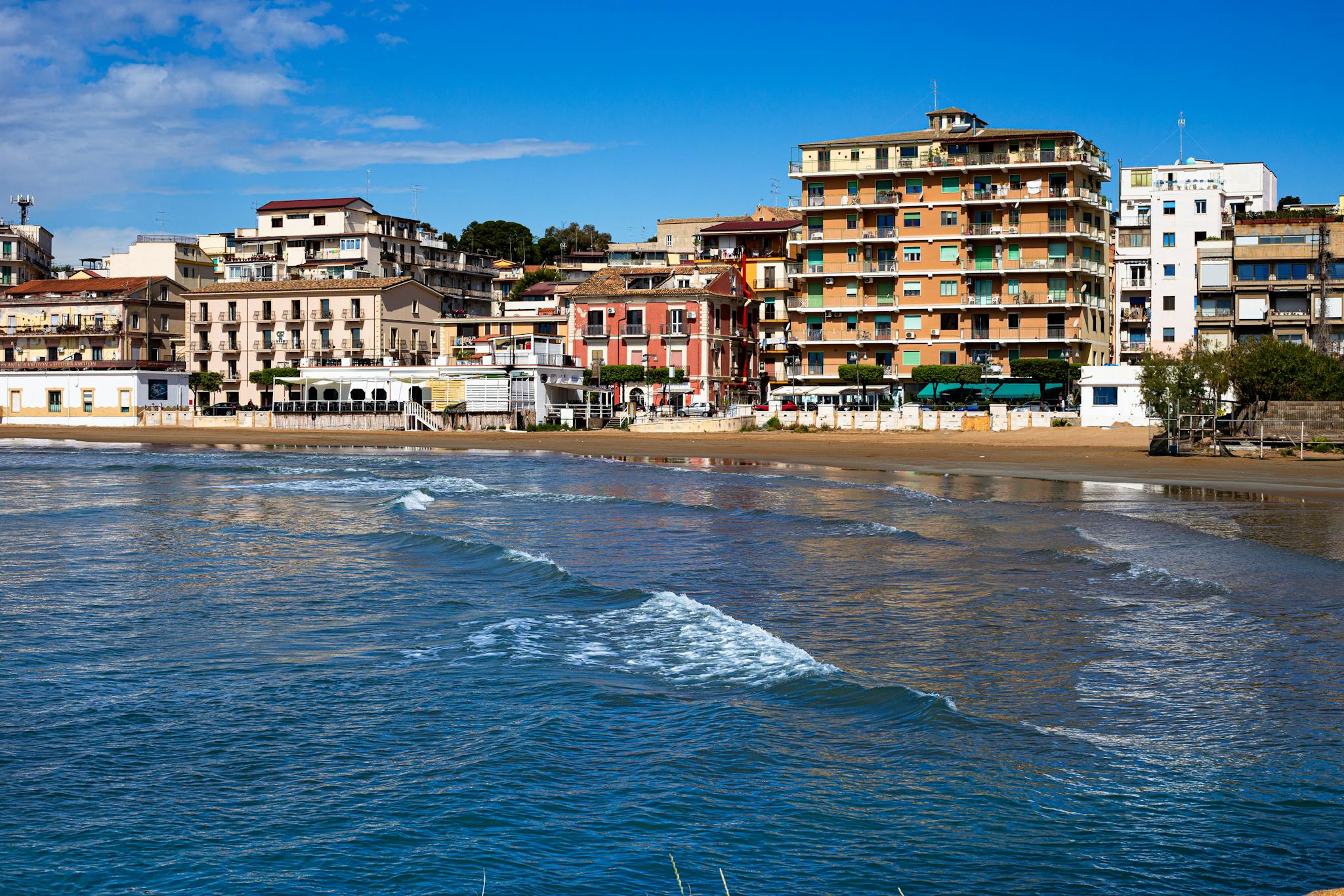 Colorful coastal townscape with vibrant buildings along the seashore under a clear blue sky.